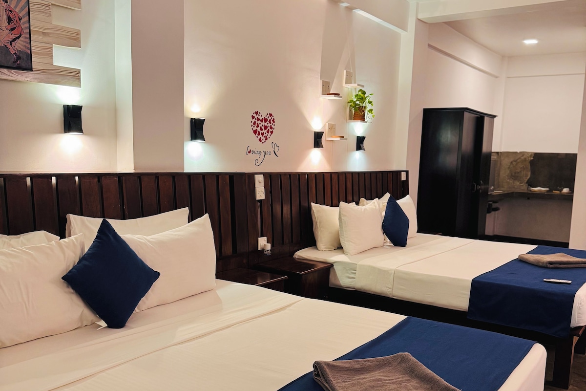 A hotel room with two beds, a dark wooden headboard, a wall with a heart-shaped decoration, and a small plant.
