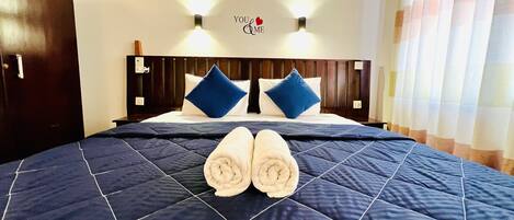 A hotel room with a bed, two wall-mounted lights, a 'You & Me' sign, and a window with curtains.