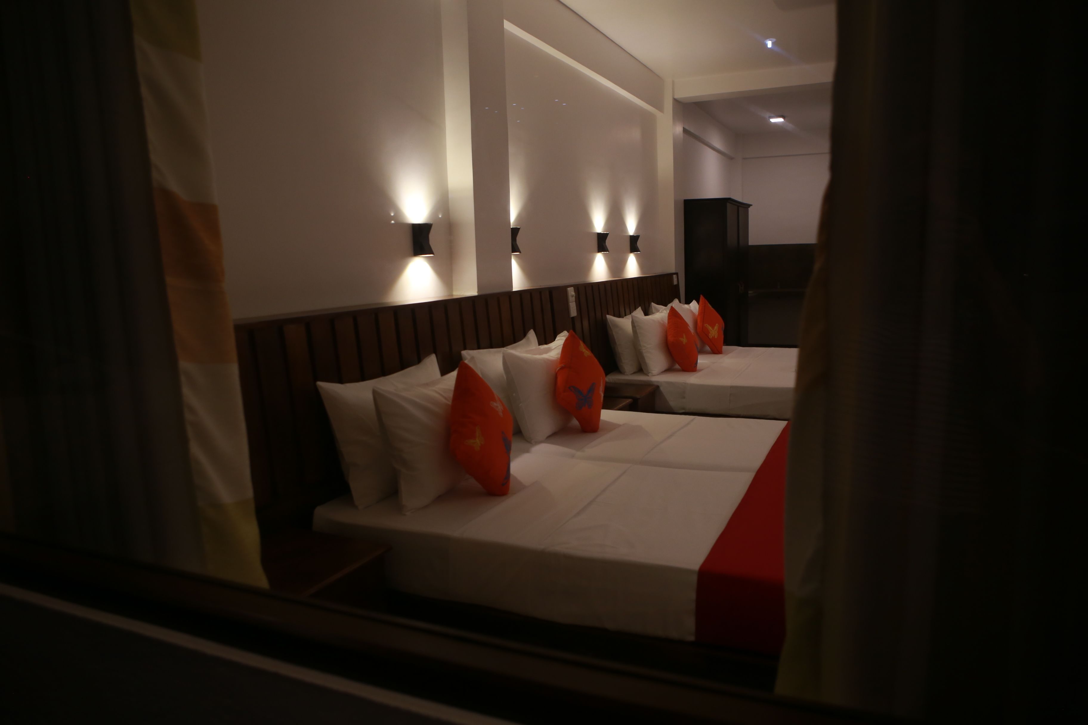 A hotel room with two beds, each with white bedding and red accents, and a large mirror above the beds.