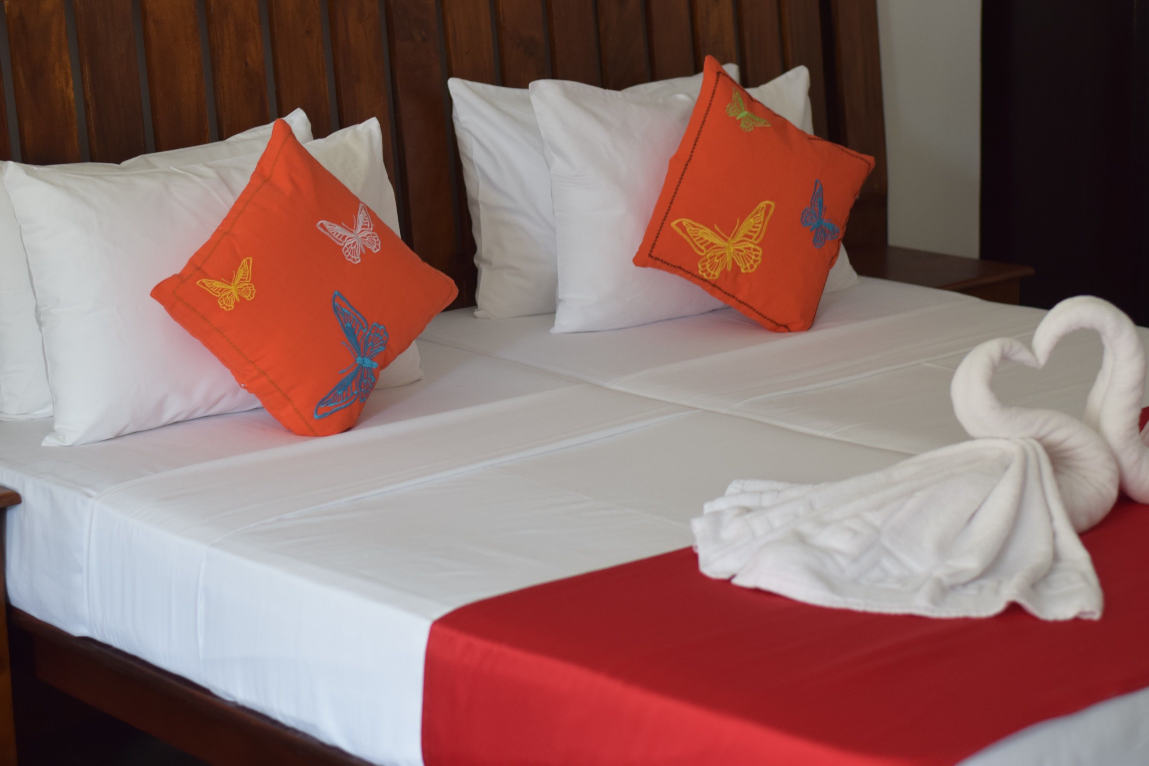 A bed with white bedding, red bedspread, and decorative orange pillows with butterfly designs.