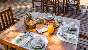 A wooden deck with outdoor dining furniture, a table set with plates, glasses, and a basket of bread. - Pousada das Araras (Petrópolis)