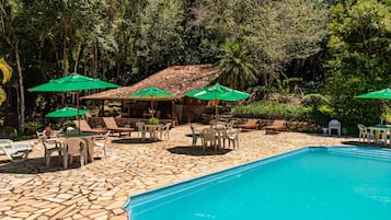 Uma área de piscina com piso de pedra, cadeiras de sol e guarda-sóis verdes.