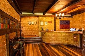 A rustic interior with a wooden bench, a curved reception desk, and a brick wall. - Pousada das Araras (Petrópolis)