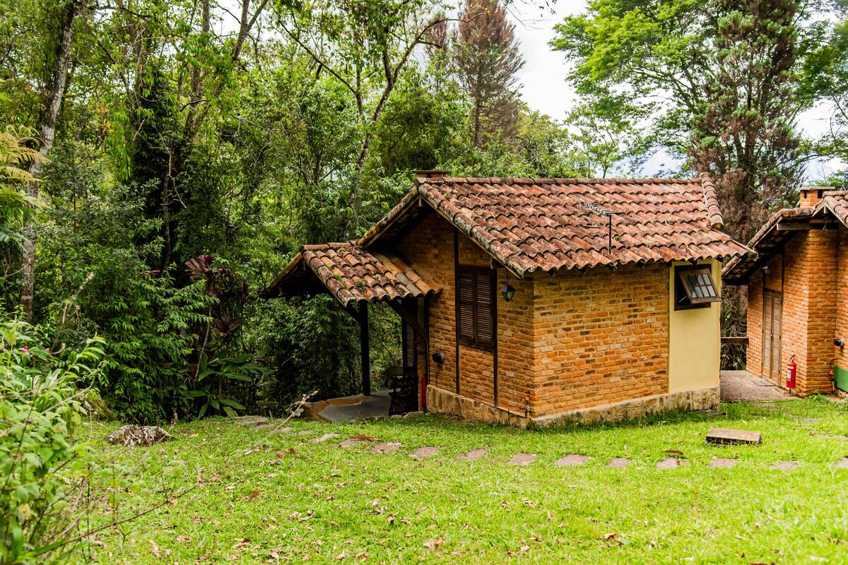 Una casa de ladrillo rústica con techo de tejas, rodeada de abundante vegetación y árboles.