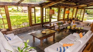 A spacious patio with a stone floor, white sofas, and a wooden coffee table. - Pousada das Araras (Petrópolis)