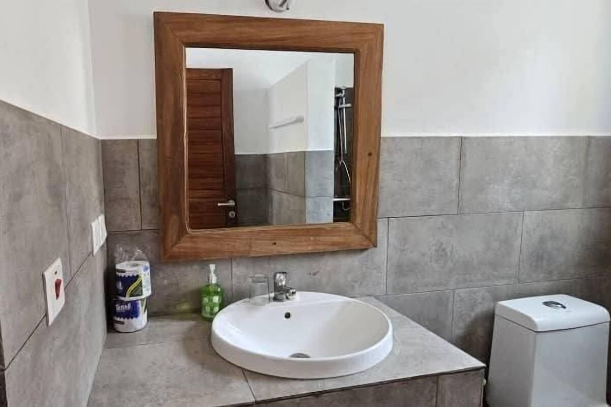 Un bany amb un mirall de fusta, un lavabo blanc i un vàter.