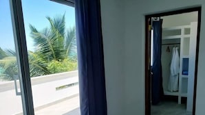 Ein Zimmer mit großem Fenster, Blick auf Palmen und einer Tür zu einem Badezimmer mit aufgehängtem weißen Handtuch.