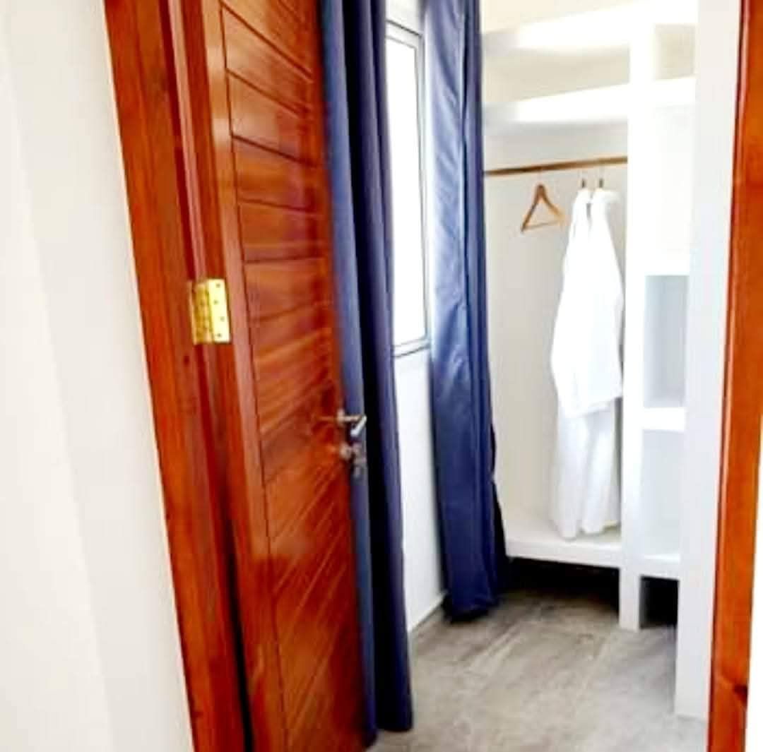 Una puerta de madera con picaporte de latón, una cortina azul y un armario blanco con ropa colgada.
