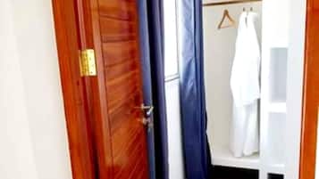 Una puerta de madera con picaporte de latón, una cortina azul y un armario blanco con ropa colgada.