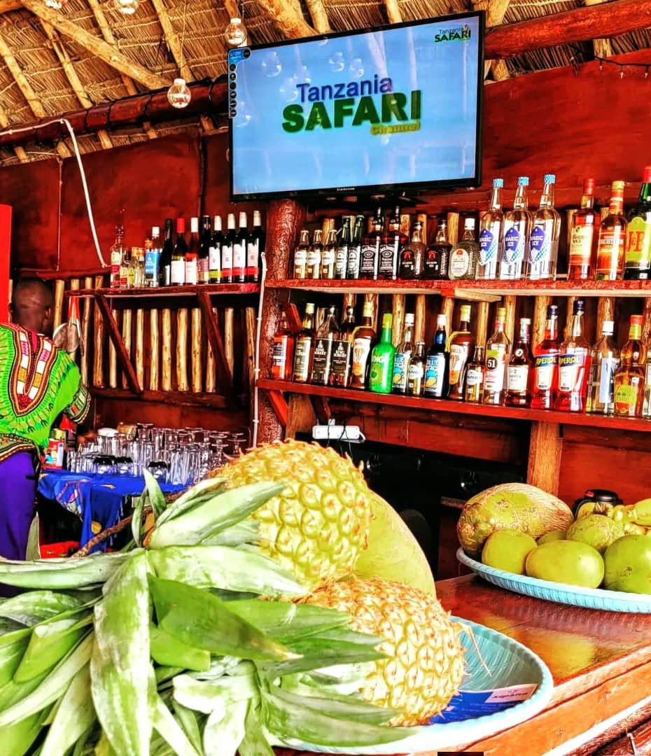 Un bar con una pantalla de televisi ón mostrando 'Tanzania Safari' y estantes llenos de diferentes botellas de licor.