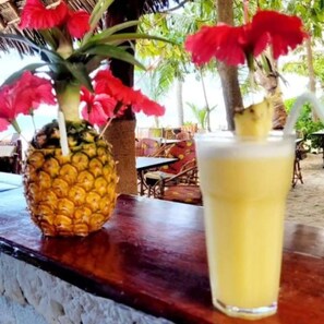 Un ananas et un verre d’une boisson jaune sont posés sur le comptoir en bois d’un bar.