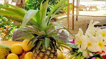 A tropical setting with a beach view, a thatched roof structure, and a variety of fruits and flowers.