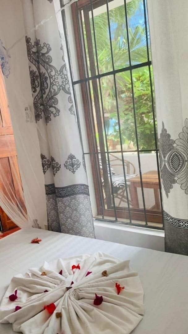 Una habitación con una cama, una ventana con barrotes y cortinas estampadas con motivos florales.