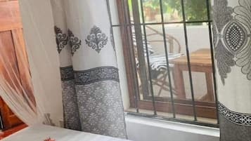 Una habitación con una cama, una ventana con barrotes y cortinas estampadas con motivos florales.