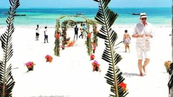 A beach wedding ceremony with a white archway and floral decorations.