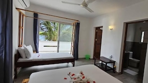 Ein Hotelzimmer mit Bett, einem kleinen Tisch, einem Deckenventilator und Blick auf Palmen.