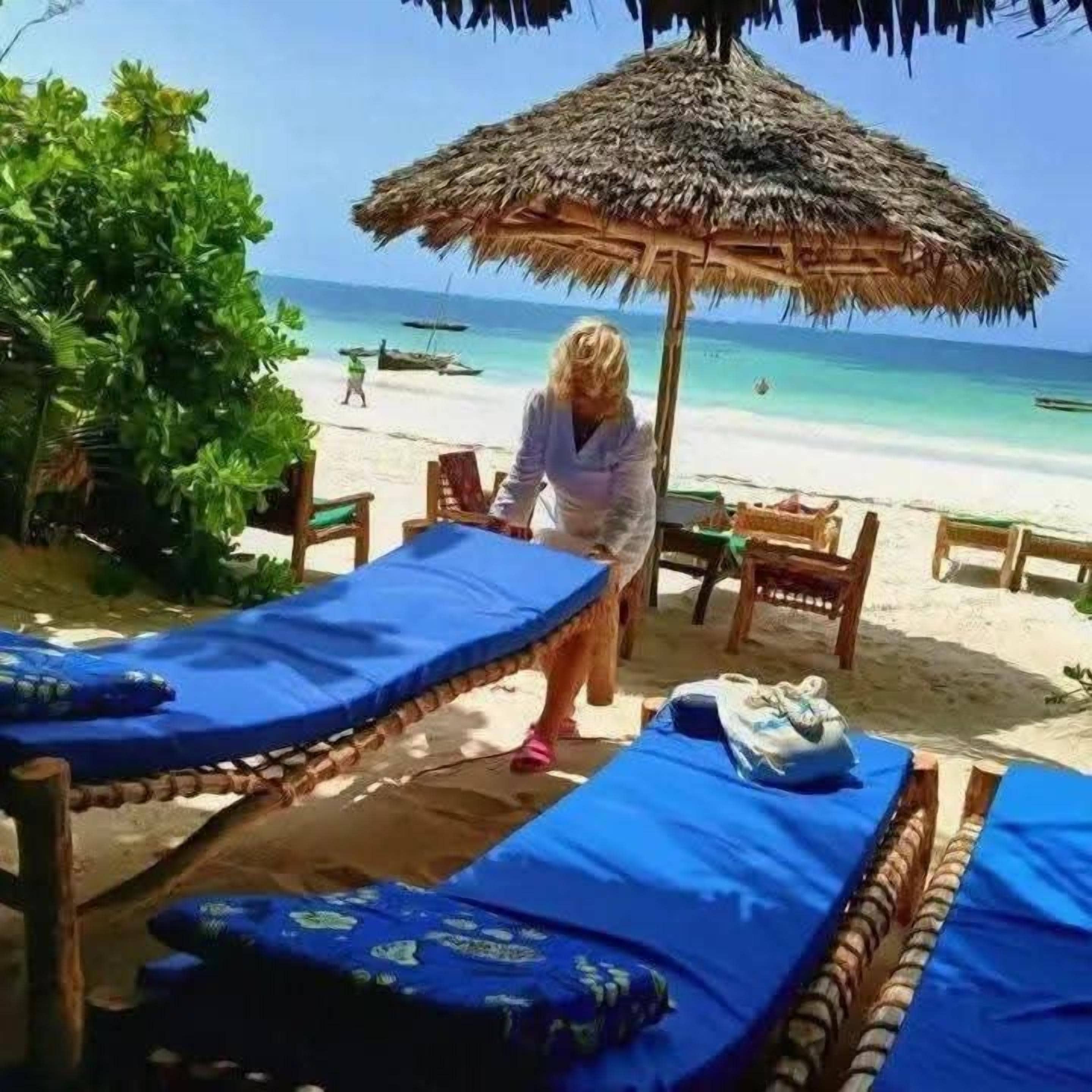 Un cadre idyllique au bord de la plage, avec des parasols en chaume, des chaises longues et une personne qui se promène.