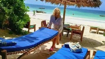 Un cadre idyllique au bord de la plage, avec des parasols en chaume, des chaises longues et une personne qui se promène.