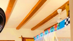 Une chambre avec un lit placé sous un dais blanc, une porte en bois et un ventilateur de plafond.