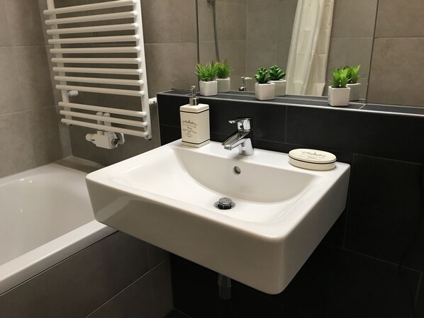 Une salle de bain avec un lavabo blanc, un miroir, un porte-serviettes et une petite plante en pot.