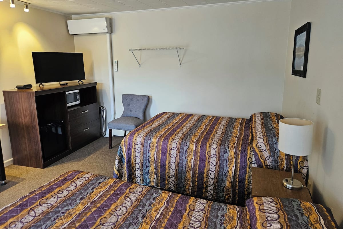 A hotel room with a bed, a chair, a desk with a TV, and a lamp.