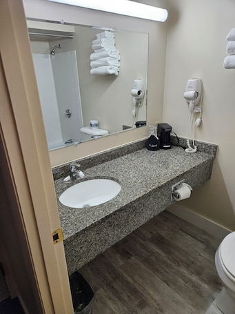 A bathroom with a granite countertop, a sink, a mirror, a towel rack, a hairdryer, and a toilet.. Brookside Inn
