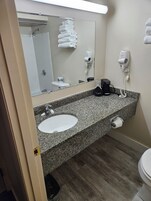 Un baño con encimera de granito, lavabo, espejo, toallero, secador de pelo y retrete.
