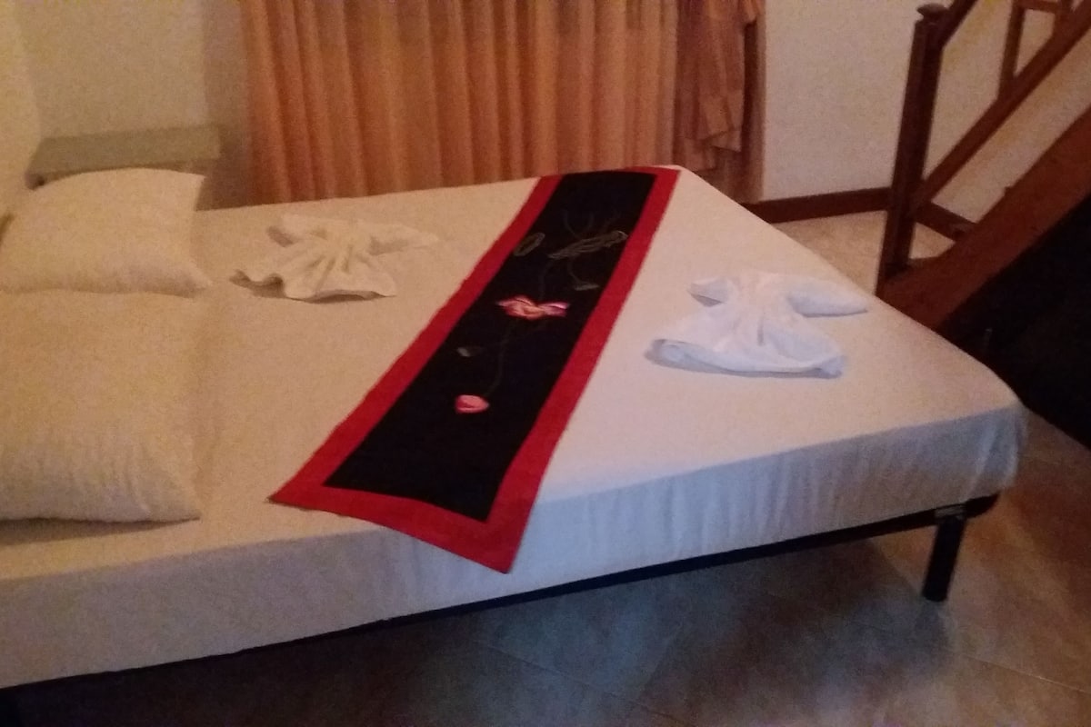 A bed with a white mattress, a red and black decorative strip, and a white towel folded on it.