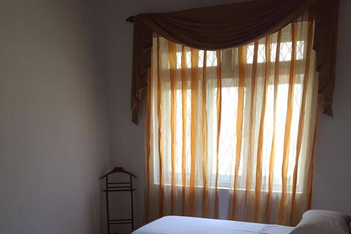 A room with two single beds, a small table, and a window with sheer curtains.