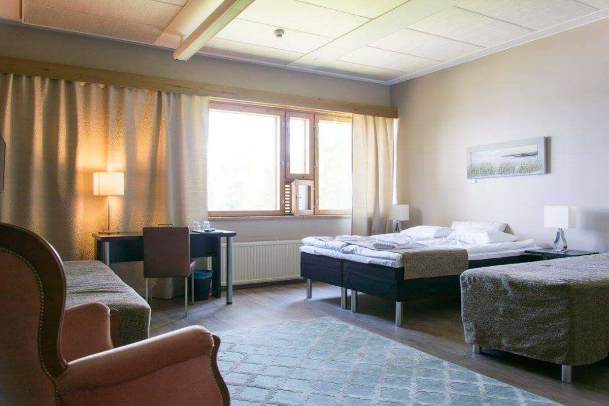 A hotel room with two beds, a desk, a chair, and a window with curtains.