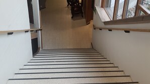 Een trap die leidt naar een lager gelegen niveau, met uitzicht op een kamer met een stoel en een schilderij aan de muur.