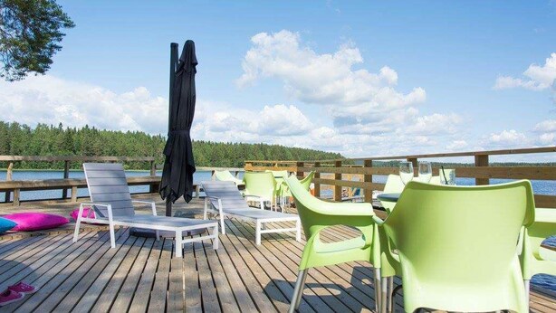 Een houten terras met ligstoelen en een tafel, met uitzicht op een waterpartij en een bos.