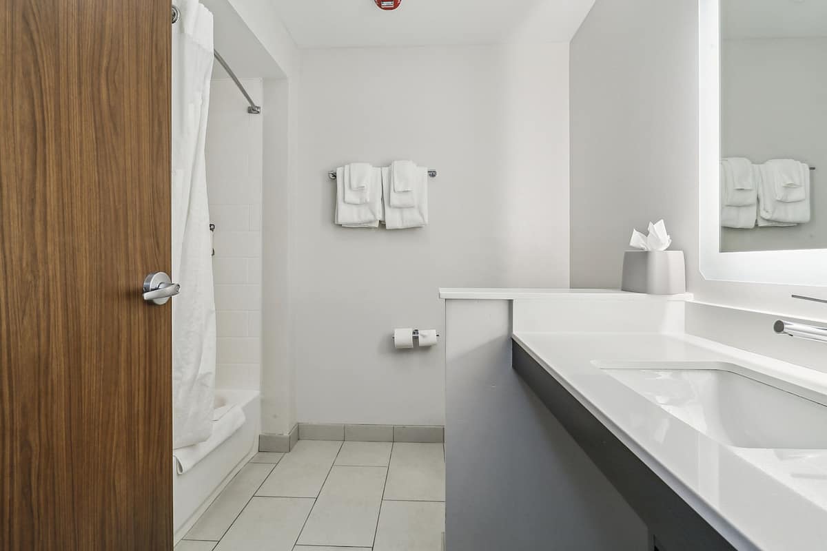 A modern bathroom with a wooden door, white tiles, a bathtub, a sink, and a mirror.
