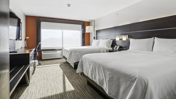 Habitación de hotel con dos camas, un escritorio, una silla, un televisor y un ventanal grande.