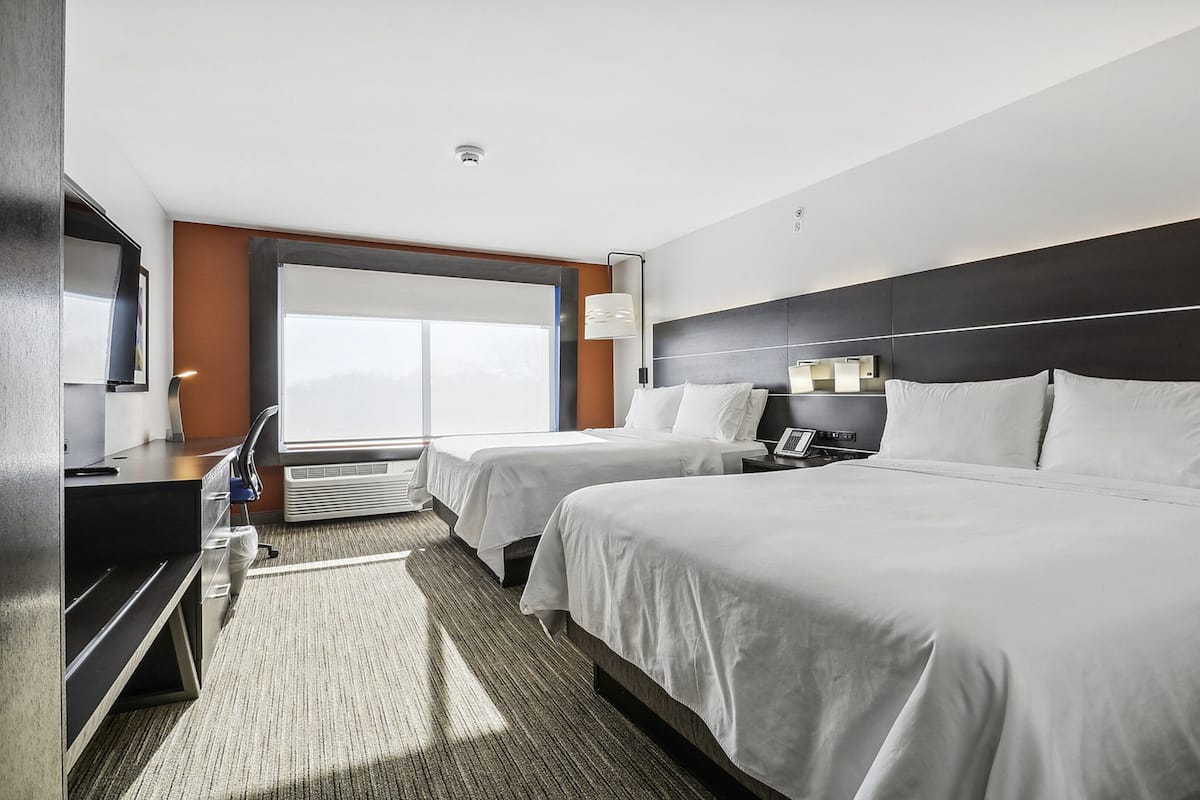 A hotel room with two beds, a desk, a chair, a TV, and a large window.