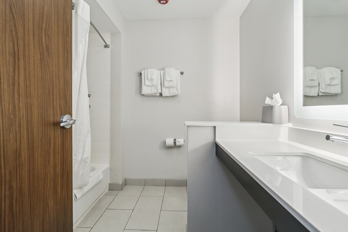 Een moderne badkamer met een houten deur, witte tegels, een bad, een wastafel en een spiegel.
