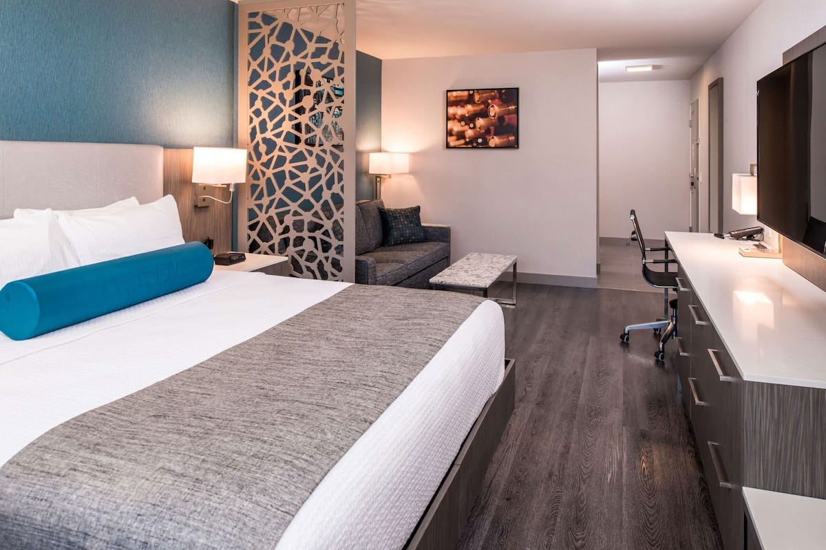 Una habitación de hotel moderna con una cama grande, un escritorio, una silla, un sofá y un panel decorativo en la pared.