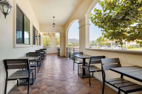 A covered outdoor seating area with hexagonal tiled flooring, black metal furniture, and a view of the cityscape.. Best Western Plus Temecula Wine Country Hotel &Suites