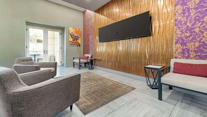 A modern lobby with a flat-screen TV mounted on a textured wall, a sofa, a coffee table, and a patterned rug. - Best Western Plus Temecula Wine Country Hotel &Suites (Temecula)