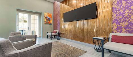 A modern lobby with a flat-screen TV mounted on a textured wall, a sofa, a coffee table, and a patterned rug.