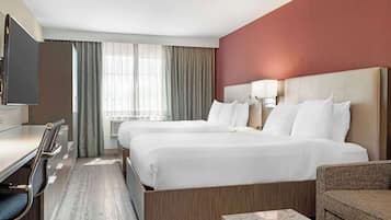 Una habitación de hotel con dos camas, un escritorio, un televisor y una ventana con cortinas.