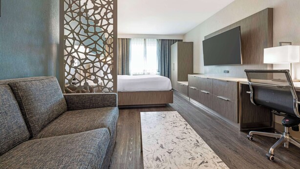 A hotel room with a sofa, a bed, a desk with a chair, a TV, and a decorative partition. - Best Western Plus Temecula Wine Country Hotel &Suites (Temecula)