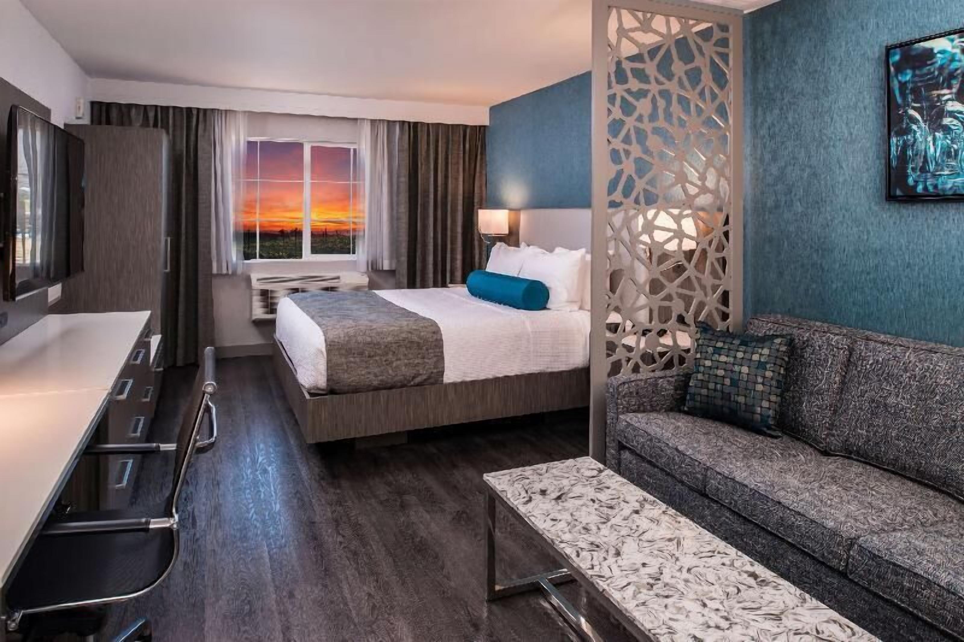 A hotel room with a bed, a sofa, a desk, and a view of the sunset.