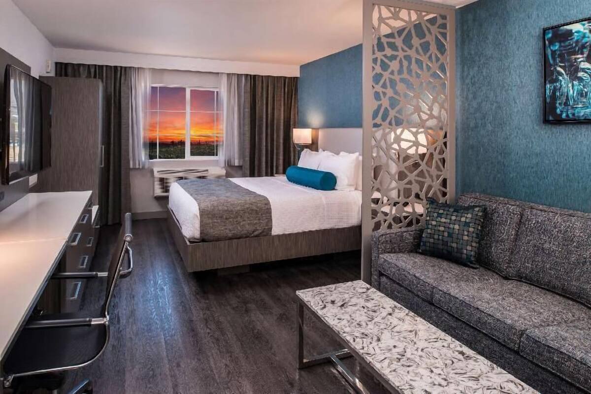 Habitaci ón de hotel con cama, sofá, escritorio y vista al atardecer.