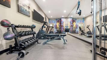 Ein Fitnessraum mit Trainingsgeräten, einem an der Wand befestigten Fernseher und einem Spiegel, der den Raum wiederspiegelt.