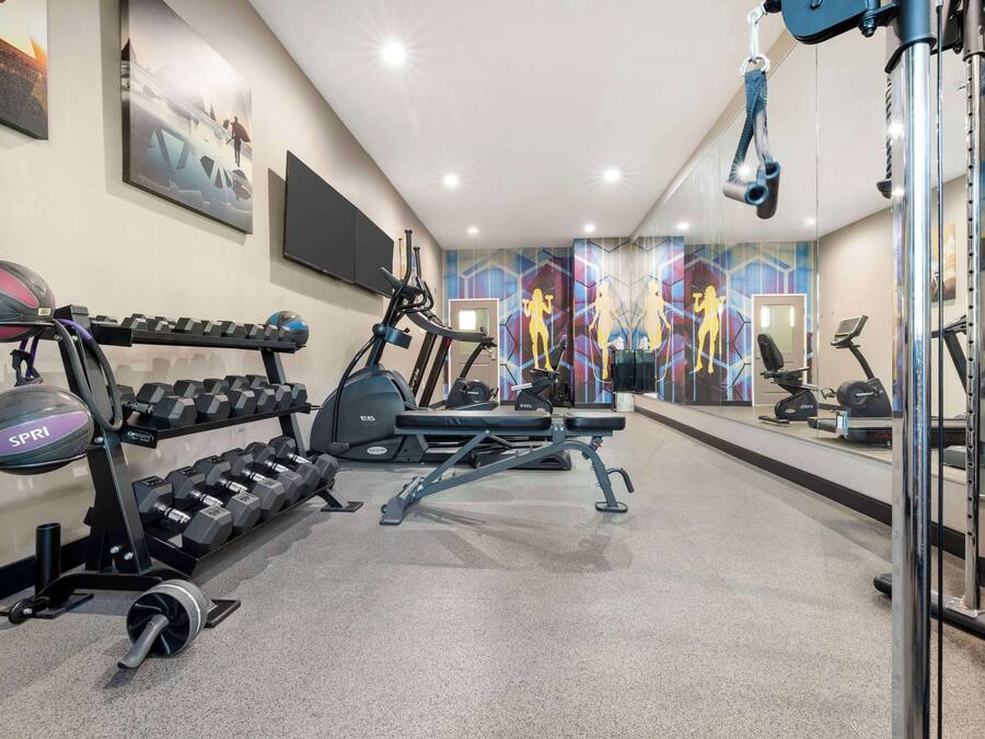 Ein Fitnessraum mit Trainingsgeräten, einem an der Wand befestigten Fernseher und einem Spiegel, der den Raum wiederspiegelt.