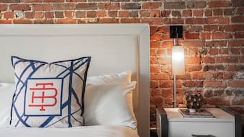 A bed with a geometric pillow design, a white nightstand with a lamp, and a brick wall background.