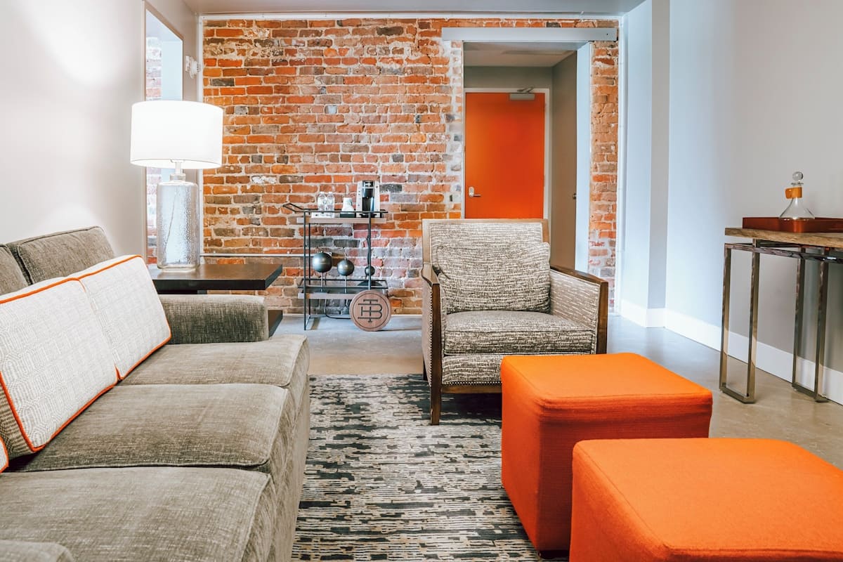 Una sala de estar moderna con una pared de ladrillo, una mesa de centro, un sofá y un reposapiés naranja.
