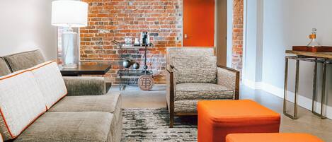 Una sala de estar moderna con una pared de ladrillo, una mesa de centro, un sofá y un reposapiés naranja.