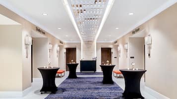 Un pasillo de hotel con alfombra azul, dos mesas redondas con velas y un mostrador de recepción central.